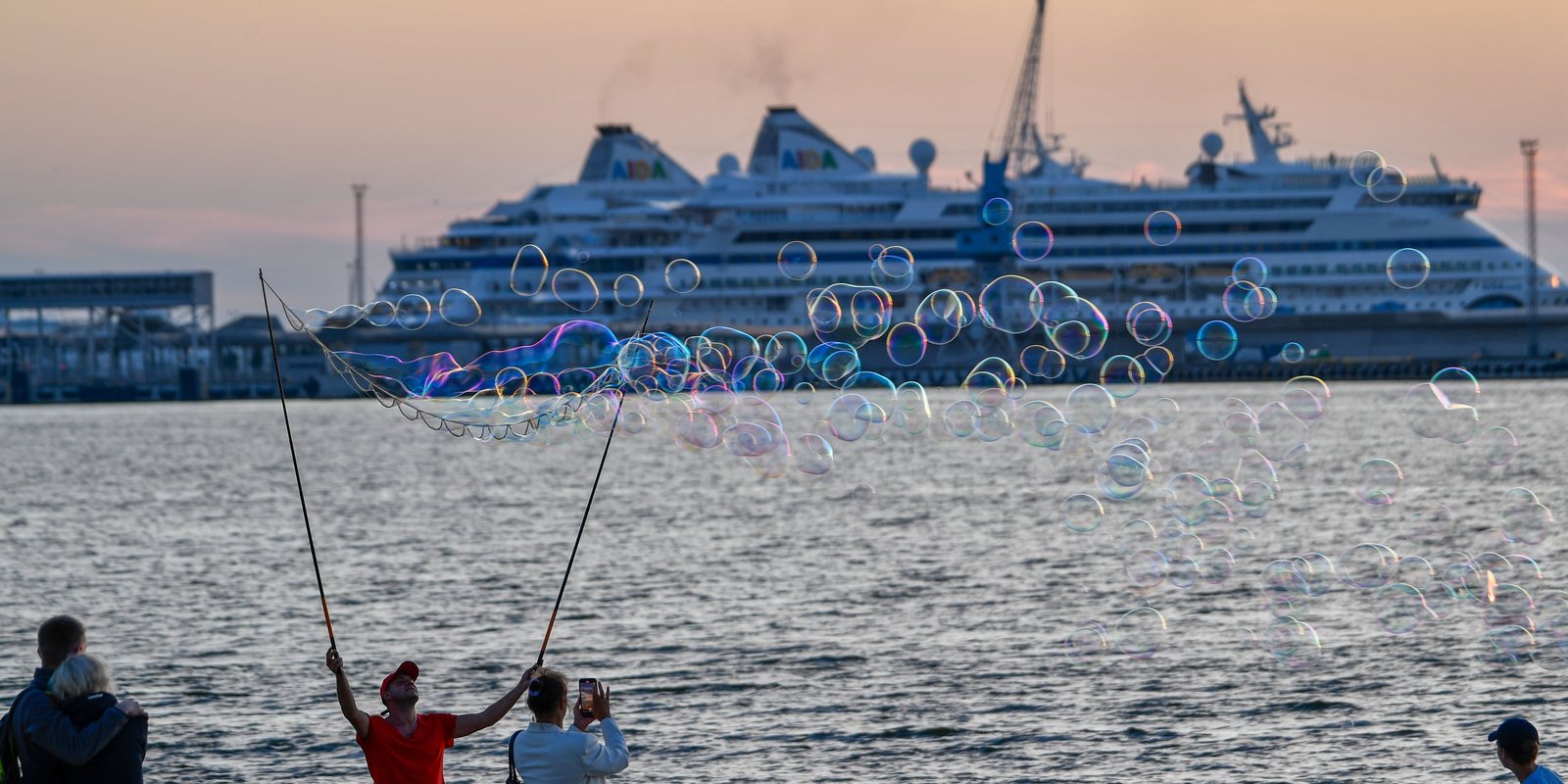 kids blowing bubbles at the port with the cruise ship behind them